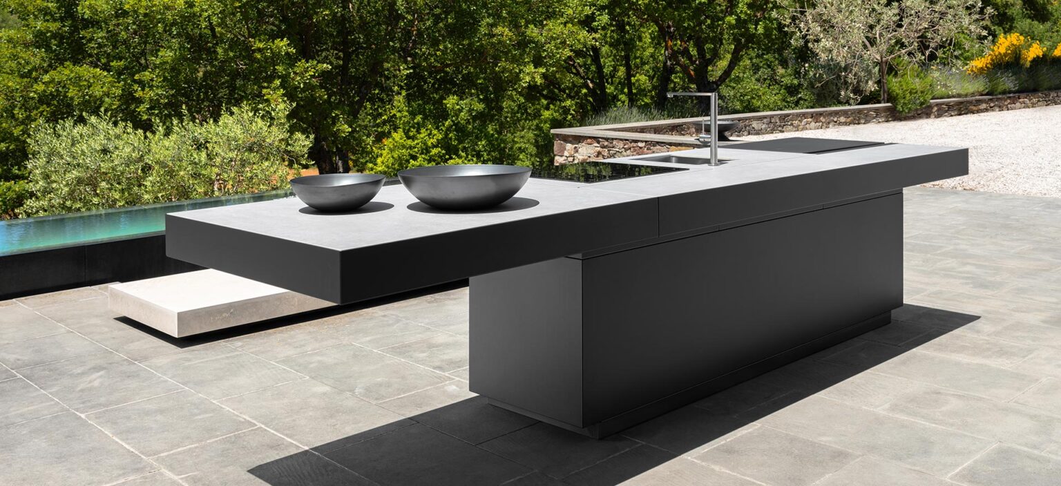 Cucina esterna di design con isola in pietra nera e piano in gres, bordo piscina